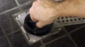 Zdjęcie przedstawiające dłoń umieszczającą syfon suchy green drain w odpływie.